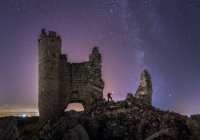 From below back view of anonymous tourist with lantern exploring ruined old castle under Milky Way at starry night — Stock Photo