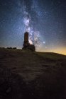 De baixo irreconhecível turista explorando arruinado castelo medieval sob céu estrelado com Via Láctea à noite — Fotografia de Stock