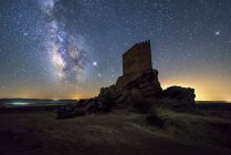 Von unten nicht wiederzuerkennender Tourist erkundet zerstörte mittelalterliche Burg unter Sternenhimmel mit nächtlicher Milchstraße — Stockfoto