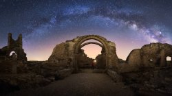 Rückansicht gesichtsloser Reisender besichtigt Reste einer antiken Burg unter der Milchstraße bei sternenklarer Nacht — Stockfoto