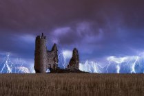 Amazing scenery of lightning storm on colorful cloudy sky over ruined old castle at night — Stock Photo