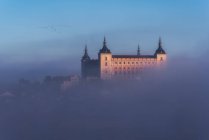 Сверху удивительный пейзаж средневекового замка, построенного над городом в туманном красочном восходе солнца — стоковое фото