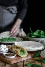 Von oben schmackhafte Tortilla mit frischem Spinatpüree auf Holzschneidebrett mit gesichtsloser Gardame auf verschwommenem Hintergrund — Stockfoto