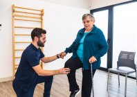 Männlicher Ausbilder unterstützt alte Frau mit Zug im Fitnessstudio — Stockfoto