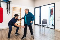 Männlicher Ausbilder unterstützt alte Frau mit Zug im Fitnessstudio — Stockfoto