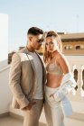 Young man in trendy suit and sunglasses and woman in trousers and bra standing close in sunlight — Stock Photo