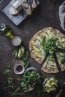 From above top view of pizza with greenery slices of squash on table with spices olive oil cheese for vegetarian dinner — Stock Photo