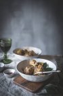 De arriba palitos de pollo guisados con caldo en tazón de cerámica blanca decorado con vegetación en la mesa con especias y bebidas - foto de stock