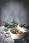 From above of stewed chicken drumsticks with broth in white ceramic bowl decorated with greenery on table with spices bread and beverage — Stock Photo