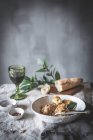 De cima de baquetas de frango cozido com caldo em tigela de cerâmica branca decorada com vegetação na mesa com pão de especiarias e bebida — Fotografia de Stock