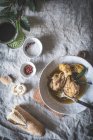 Vista superior de baquetas de frango cozido com caldo em tigela de cerâmica branca decorada com vegetação na mesa com pães de especiarias e bebidas — Fotografia de Stock