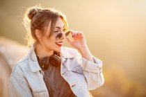 Fröhliche junge Frau mit Sonnenbrille im trendigen lässigen Outfit lächelt und schaut an sonnigen Tagen weg — Stockfoto