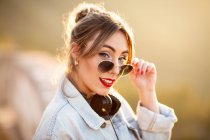 Joyful young woman with sunglasses in trendy casual outfit smiling and looking at camera on sunny day — Stock Photo
