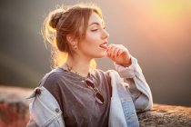 Fröhliche junge Frau im trendigen lässigen Outfit lächelt und schaut an sonnigen Tagen weg — Stockfoto