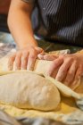 From above of faceless female hands kneading bunch of fresh dough at table in bakery — Stock Photo