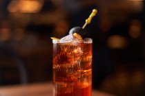 Copo Highball com coquetel de álcool vermelho com cubos de gelo decorados com pau com azeitona preta no balcão de madeira — Fotografia de Stock