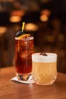 Cocktail con cubetti di ghiaccio decorato con bastoncino con olive nere e Whiskey Sour con succo di limone cocktail su bancone in legno — Foto stock