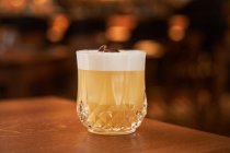 Glass of classic alcohol cocktail Whiskey Sour with lemon juice and egg white placed on wooden counter — Stock Photo