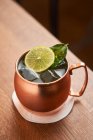 From above classic alcohol cocktail Moscow Mule based on vodka with ginger beer and lime juice served in copper mug decorated with lemon slice on wooden table — Stock Photo