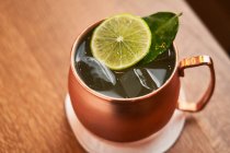D'en haut cocktail d'alcool classique Moscou Mule à base de vodka avec bière au gingembre et jus de citron vert servi dans une tasse en cuivre décorée avec une tranche de citron sur une table en bois — Photo de stock