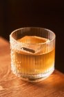Короткий стакан коктейля из янтарного алкоголя со льдом, украшенный сахаром на деревянном столе на черном фоне — стоковое фото