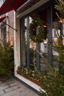 Facciata di caffè con decorazioni colorate di rami di conifere e albero di Natale con ghirlande alla luce del giorno — Foto stock