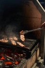 Crop chef transformando tiras de bacon suculento grelhar enquanto cozinha com fumaça no rack no jardim — Fotografia de Stock