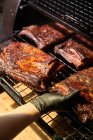 De dessus de chef de culture dans des gants griller morceaux de viande dans sur rack dans le barbecue — Photo de stock