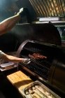 De arriba del cocinero de cosecha en guantes asar trozos de carne en el estante en la barbacoa - foto de stock