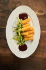 Draufsicht auf frittierte Käsesticks mit Gurkenscheiben und Barbecue-Sauce auf Teller auf Holztisch — Stockfoto