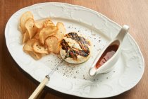 Von oben köstliche gegrillte Chicken Burger mit knusprig gebackenen Brotchips und BBQ-Sauce auf dem Teller auf dem Tisch — Stockfoto