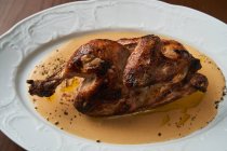 De frango inteiro grelhado saboroso cozido acima servindo na placa branca na mesa — Fotografia de Stock