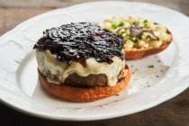 De arriba la hamburguesa sabrosa de vaca abierta con el queso y la salsa de barbacoa en el plato a la mesa - foto de stock