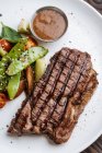Von oben Blick auf gegrilltes Rindersteak mit Basilikum und Gemüse auf Teller mit BBQ-Sauce — Stockfoto