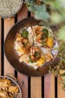 Зверху смачні свіжі смажені яйця з креветками, покритими травами на сковороді на дерев'яному столі в саду — стокове фото