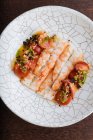 Von oben schmackhafte Garnelen mit rot geschnittenen Tomaten bestreut mit Sesam und Kräutern auf weißem Zierteller — Stockfoto