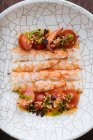 D'en haut, de savoureuses crevettes aux tomates rouges tranchées saupoudrées de graines de sésame et d'herbes sur une assiette décorative blanche — Photo de stock