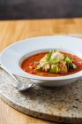 Красный аппетитный свежий томатный суп с зеленью на белой тарелке на мраморном столике в кафе — стоковое фото
