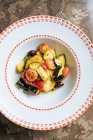 Dall'alto insalata vegetale fresca succosa di carota di cavolfiore di pomodoro con verde in piatto bianco ornamentale su tavolo rotondo in ristorante — Foto stock