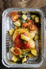 Von oben reife Scheiben rote Tomaten Zucchini mit Kräutern und Soßen in glänzender Backform auf den Tisch streuen — Stockfoto