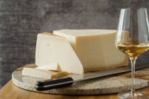 Bloco apetitoso gourmet de faca de queijo na tábua de corte e vinho em vidro na mesa — Fotografia de Stock