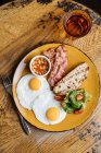 From above appetizing fried eggs bacon corn in tomato greens on yellow plate in with drink in cafe — Stock Photo