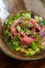 Свежий салат из лосося в соусе с зеленью на миске на столе — стоковое фото