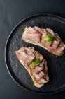 Von oben saftig schmackhafter Schinken auf knusprigen Toasts auf schwarzem Teller auf Holztisch im Restaurant — Stockfoto
