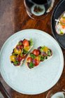 De cima festivo decorado sanduíches coloridos com vermelho amarelo em fatias de tomate cereja e ervas em placa branca com vinho na mesa — Fotografia de Stock