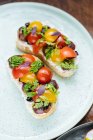 From above festive decorated colorful sandwiches with red yellow sliced cherry tomatoes and herbs on white plate — Stock Photo