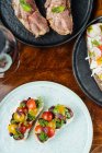 Сверху празднично украшенные красочные бутерброды с красно-желтыми нарезанными помидорами черри и травами на белой тарелке с вином на столе — стоковое фото