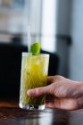 Hand o beschnitten unkenntliche Person trinkt leckere appetitlich gekühlte Limonade mit Minze und Stroh auf dem Tisch im Sonnenlicht — Stockfoto