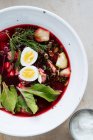 Зверху приємний червоний буряковий суп з вареними яйцями і травами в білій тарілці на столі — стокове фото