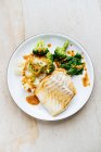 Apetitivo pescado fresco con verde y brócoli espolvoreado con salsa roja en el plato blanco - foto de stock